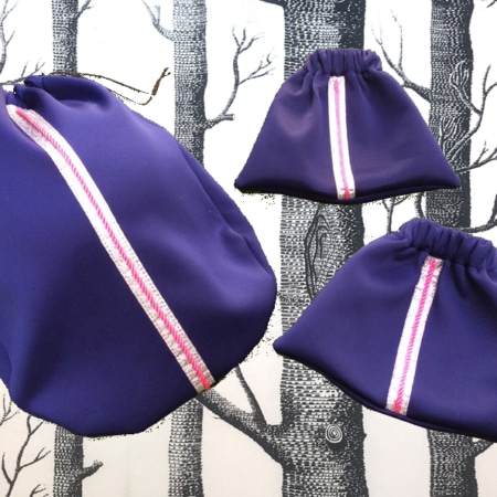 L'ensemble « sport chic » se compose de trois sacs à cordon violets aux accents rayés roses, élégamment mis en valeur sur un motif d'arbre noir et blanc, ajoutant du charme à votre collection d'accessoires.