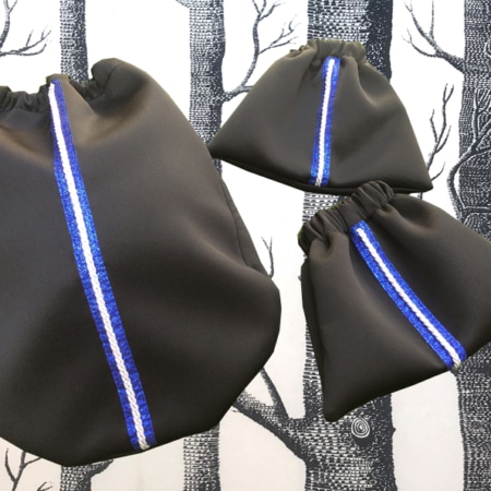 L'ensemble « sport chic » se compose de trois sacs à cordon noirs à rayures verticales bleues et blanches rappelant le style équestre, sur un fond noir et blanc à motifs d'arbres. Ils sont les accessoires parfaits pour une balade chic à Lyon.