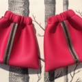 Deux pochettes rouges de la collection « Ensemble « sport chic » » aux rayures métallisées se détachent avec élégance sur un fond monochrome à motifs d'arbres, incarnant les accessoires stylés et chics de Lyon.