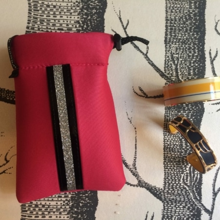 Une Mini housse « Sport chic », un ruban coloré et un bracelet noir-or reposent élégamment sur une surface à motifs d'arbres, comme s'ils étaient exposés dans un charmant magasin.