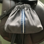 La pochette Housses d’étriers « sport chic », aux rayures bleues et blanches, repose élégamment sur un sac en cuir marron.