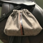 Les « Housses d’étriers « sport chic », un sac en tissu gris avec cordon de serrage et bande marron, reposent élégamment sur une selle en cuir noir, ce qui en fait l’accessoire parfait pour tout passionné d’équitation.