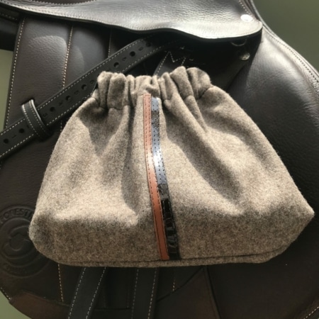 Les « Housses d’étriers « sport chic », un sac en tissu gris avec cordon de serrage et bande marron, reposent élégamment sur une selle en cuir noir, ce qui en fait l’accessoire parfait pour tout passionné d’équitation.