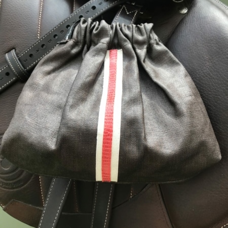 La Housses d’étriers « sport chic » est un sac à cordon noir de style cavalier présentant une bande verticale rouge et blanche saisissante, élégamment placée sur une surface en cuir.