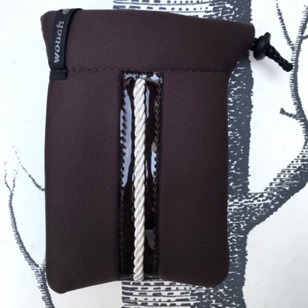 Pochette marron "Housses d’étriers « sport chic »" avec un détail de corde sur le devant, évoquant un accessoire élégant pour le cavalier moderne, sur fond à motifs noir et blanc.